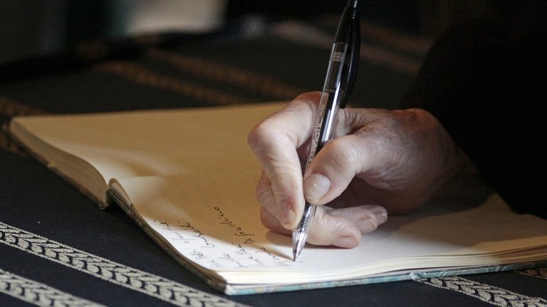 Eine Hand hält einen Kugelschreiber und schreibt in ein Buch