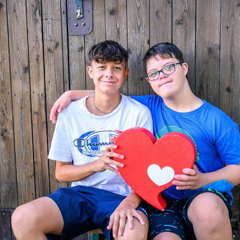 Zwei Jungen halten gemeinsam das Herzenssache-Herz und lächeln in die Kamera