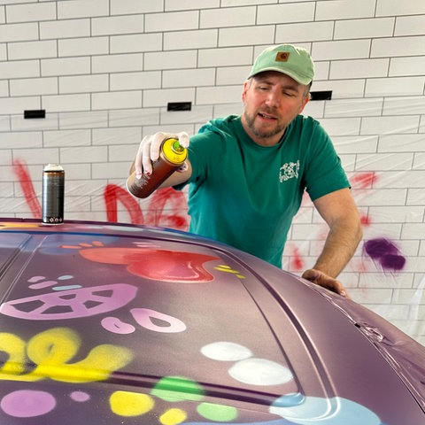 Grafitti-Künstler Till Jürgens sprayt den Herzenssache-Bus