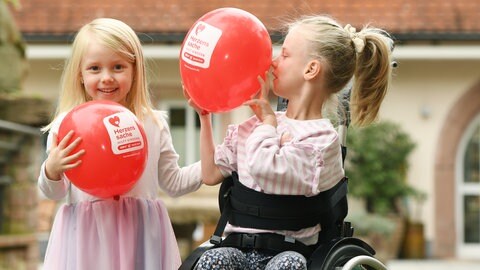 Zwei Mädchen mit roten Luftballons, eins schaut in die Kamera (Foto: Carsten Costard) Zwei Mädchen mit roten Luftballons, eins schaut in die Kamera