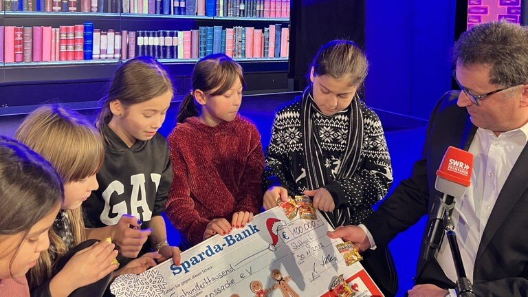 Foto: Herzenssache e.V. Drei Herzenssache-Kids sitzen auf einer Bühne, daneben sitzt Martin Hettich von der Sparda-Bank Baden-Württemberg (Foto: Herzenssache e.V.)