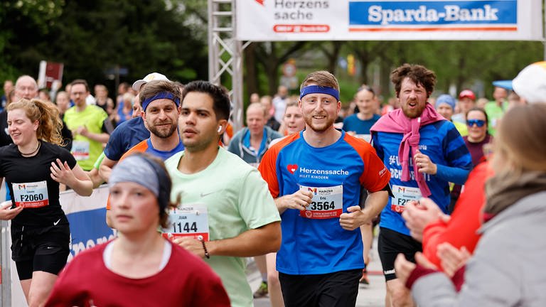 Menschen laufen beim Mainzer Gutenberg Halbmarathon durch das Herzenssache-Spendentor
