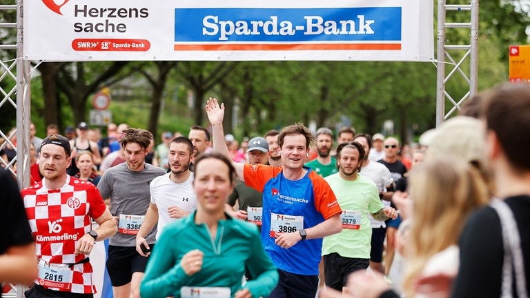 Menschen laufen beim Mainzer Gutenberg Halbmarathon durch das Herzenssache-Spendentor