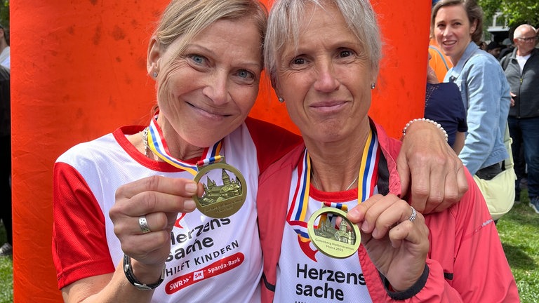 Zwei Läuferinnen im Herzenssache Laufshirt und Medaillen (Foto: Herzenssache e.V.) Zwei Läuferinnen im Herzenssache Laufshirt und Medaillen