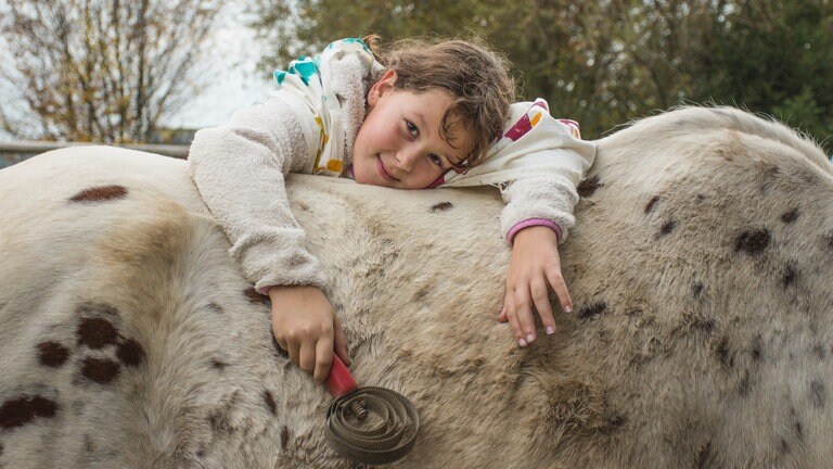 Mädchen liegt auf dem Rücken eines Pferdes (Foto: Herzenssache)