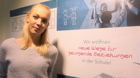 Foto: Herzenssache Junge Frau steht vor Plakat (Foto: Herzenssache)