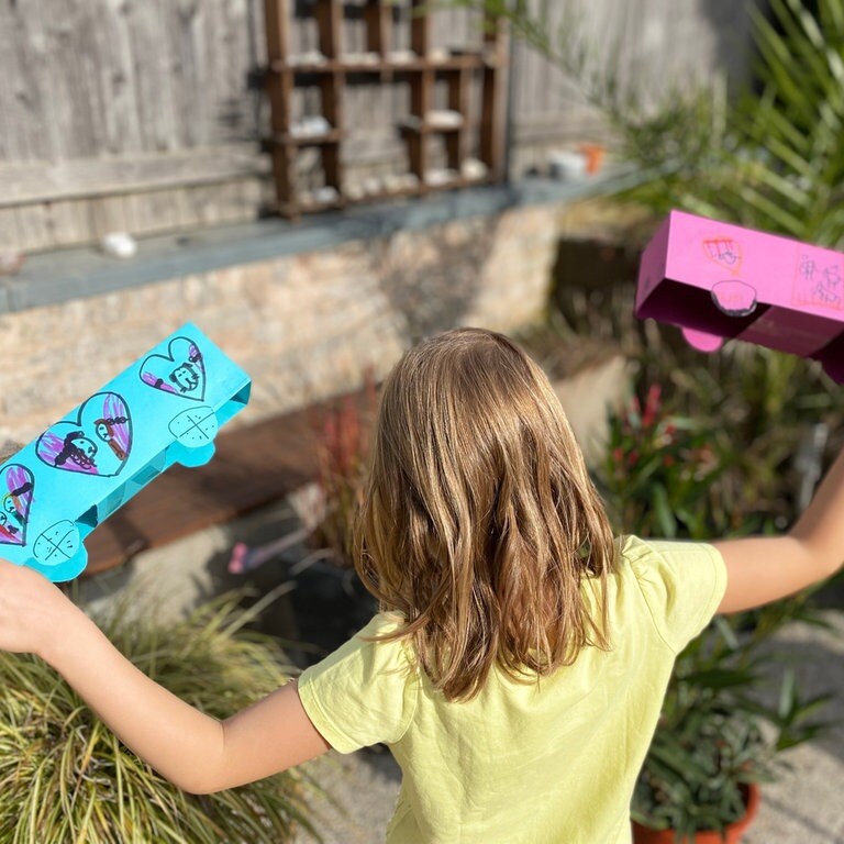 Herzenssache-Projekt Löwenzahn Mädchen (von hinten zu sehen) spielt mit zwei Papierautos (Foto: Herzenssache)