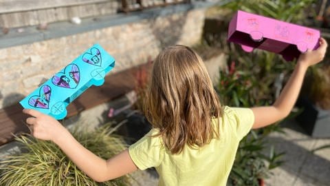 Herzenssache-Projekt Löwenzahn Mädchen (von hinten zu sehen) spielt mit zwei Papierautos (Foto: Herzenssache)