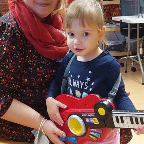 Kind mit Spielzeug-Gitarre auf dem Schoß einer Frau (Foto: Herzenssache)