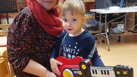 Kind mit Spielzeug-Gitarre auf dem Schoß einer Frau (Foto: Herzenssache)