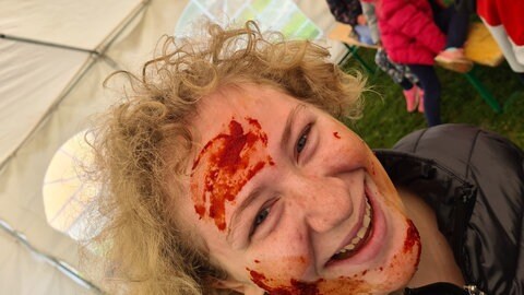 Foto: Herzenssache lachendes Mädchen, mit rot-braun verschmiertem Gesicht im Vordergund. Im Hintergrund sitzen weitere Kinder auf einer Bank. (Foto: Herzenssache)