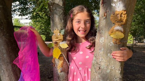 Foto: Herzenssache Lachendes Mädchen mit Tuch hinter einem Baum (Foto: Herzenssache)