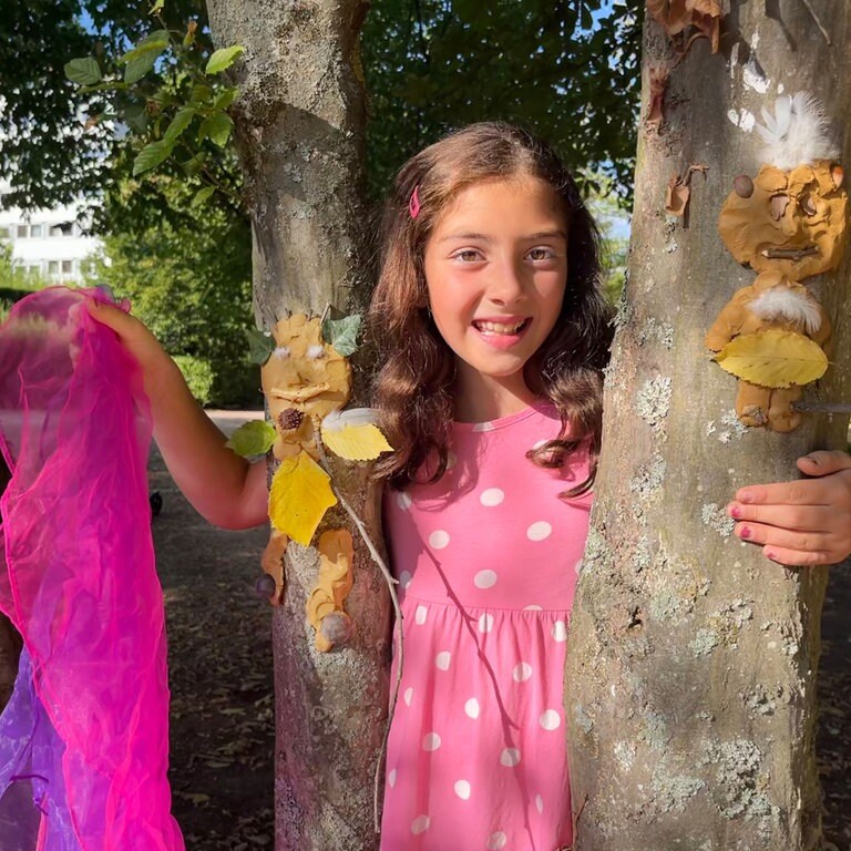 Lachendes Mädchen mit Tuch hinter einem Baum (Foto: Herzenssache)