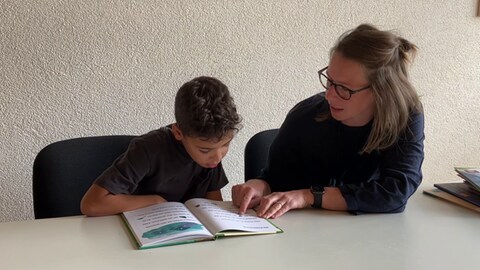 Foto: Herzenssache e.V. Junge sitzt mit Lesepatin an einem Tisch (Foto: Herzenssache e.V.)