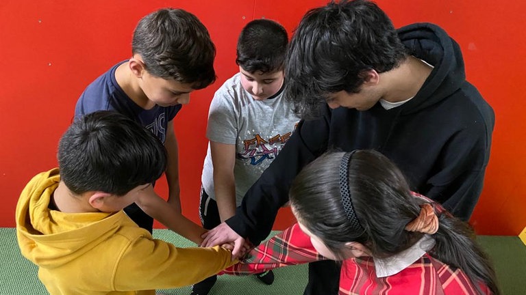 Kinder und Jugendliche stehen im Kreis, die Hände liegen in der Mitte aufeinander (Foto: Herzenssache)