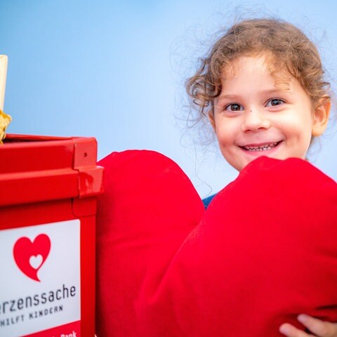 Mädchen hält rotes Herz in der Hand und schaut verträumt (Foto: Marcel Katz)