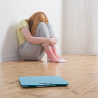 Mädchen sitzt verzwefelt hinter einer Waage