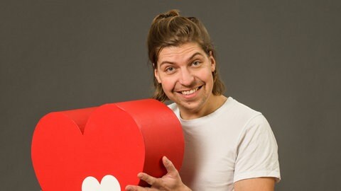 Philipp Poisel hält ein großes Herz in der Hand. Das Hers ist das Symbol der Herzenssache.