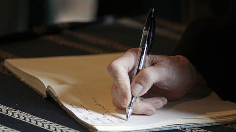 Eine Hand hält einen Kugelschreiber und schreibt in ein Buch (Foto: Pixaby)