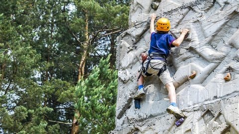 Junge im blauen Shirt klettert an einer Kletterwand